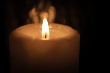 Burning thick candle closeup in a dark church room