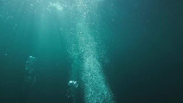 Slow-motion underwater footage moving through rising air bubbles in deep blue ocean water. Abstract marine scene with dynamic motion and natural light refraction.