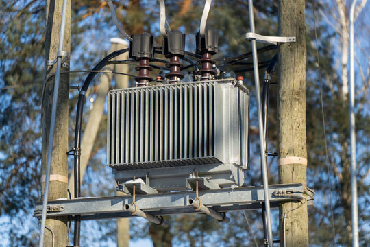 Detailed view of electrical transformer box on utility pole, insulated connectors and wiring on metal cross arm, energy grid equipment in daylight