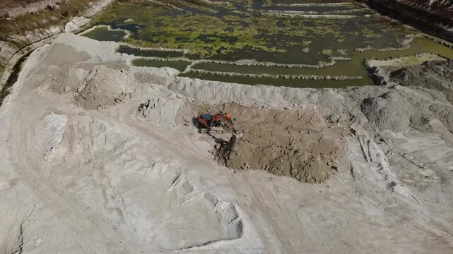 Aerial drone close-up of excavator digging and loading material inside active borrow pit