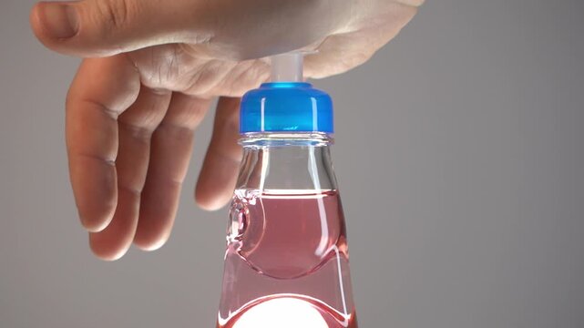 Close-up of a hand opening a traditional glass bottle of pink carbonated soda with a special plunger cap. Refreshing summer drink in a studio setting, soft beverage concept.