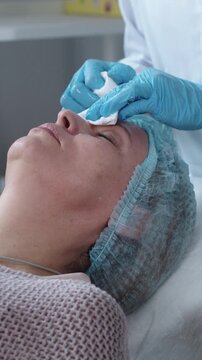 Cosmetology treatment - cosmetologist wiping the facial skin of her female client