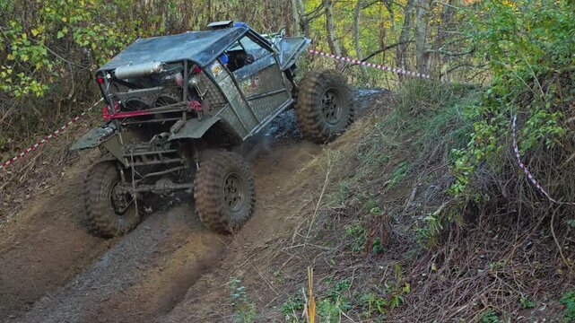 Extreme off-road competition with a custom 4x4 buggy climbing a difficult, muddy hill. The powerful vehicle navigates challenging terrain in a forest setting. Slow motion