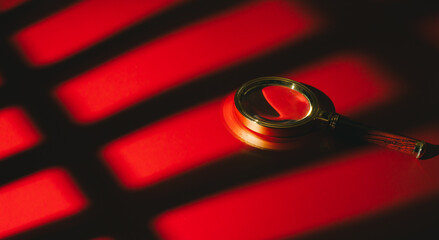 Search concept. Magnifying glass on red surface with shadow pattern creating dramatic and mysterious atmosphere
