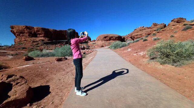 Woman on vacation standing on trail and bushes taking photos of unique formation of red sand sandstone at Pioneer Park in Utah