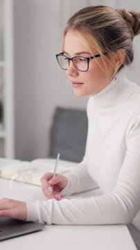 A woman studies on a laptop while taking notes in a cozy indoor space.
