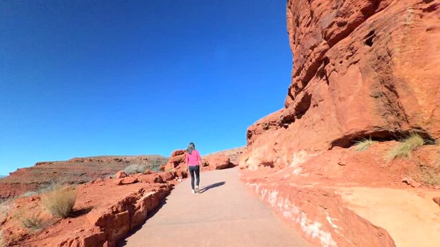 Woman on vacation walking on trail near vibrant red boulders of unique formation sandstone with deep blue sky at Pioneer Park in Utah