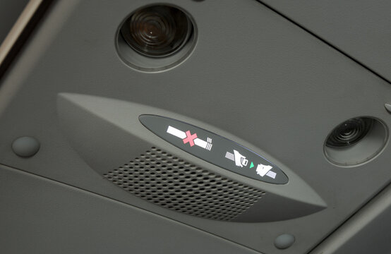 buckle seatbelt and no smoking sign lit up on airplane overhead air valve flying plane travel business leisure grey interior inside ceiling