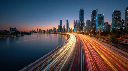 Fotobehang Snelweg bij nacht Modern city skyline at dusk with long exposure light trails on a highway next to a river  © AR