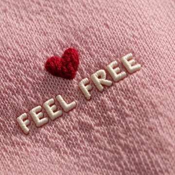 Primer plano de una tela rosa con bordados que dicen 'Feel Free' y un coraz&oacute;n rojo.
