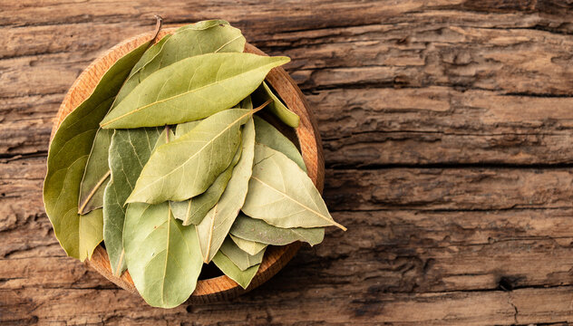 Bay leaves on a bowl against an wooden table background.	