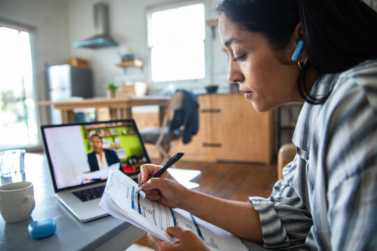 Focused woman on video call completing paperwork at home kitchen