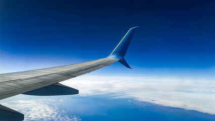 Fototapeta premium Airplane wing above the clouds and blue sky. View from inside airplane window. Travel and vacation concept