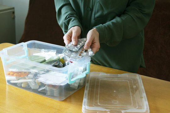 Person reviewing medication blisters near transparent organizer in calm domestic setting. Represents chronic condition self-management, long-term treatment adherence, and  healthcare decisions.