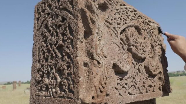 A restoration expert carefully cleaning the intricate carvings and geometric patterns of a medieval Seljuk tombstone using professional brushes and tools in Ahlat, Turkey.