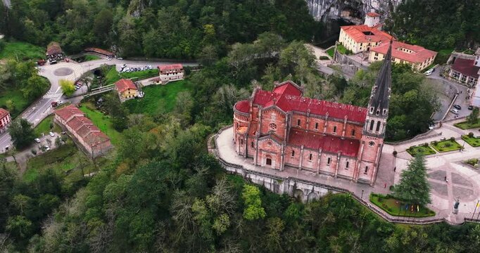 High drone panorama of Covadonga church basilica, sanctuary and surrounding Asturias mountains, capturing Spanish religious landmark, forested slopes and dramatic terrain