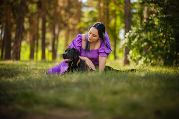 Fototapeta premium Harmony of nature: A woman in a purple dress walks her dog in the forest. Time with a beloved pet.