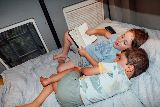Young brothers reading book together in camper van bunk