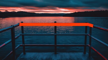 Vibrant orange sunset casts a fiery glow across a tranquil lake with a reflective barrier in the foreground