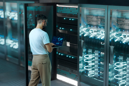 Man analyzing network performance on laptop inside digital 3D data center
