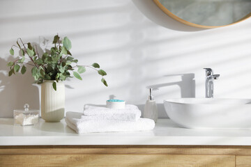 Stack of clean towels and cosmetic products on vanity in bathroom © New Africa