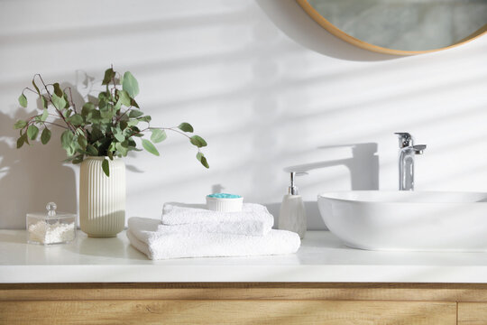 Stack of clean towels and cosmetic products on vanity in bathroom