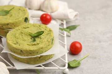 Uncooked chickpea patties with spinach and tomatoes on gray textured table, closeup. Space for text
