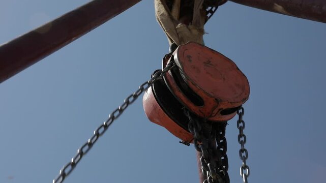 Manual chain hoist mechanism used for lifting heavy stone blocks during restoration at the Ahlat Seljuk Square Cemetery. Close-up of the technical restoration process against a clear blue sky.