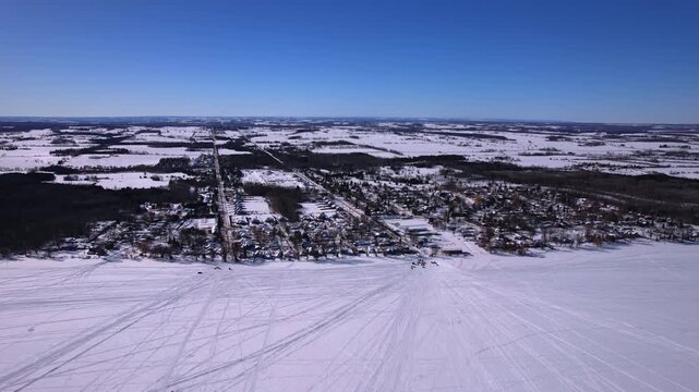 Aerial drone footage of snowmobiles intricate curved tracks patterns textures on fresh winter snow under bright sunny sunlight. Ice fishing sport on frozen lake Simcoe, Cook&rsquo;s Bay, Innisfil, Canada.