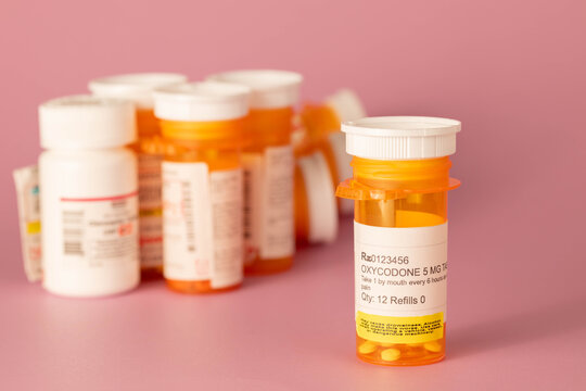 Oxycodone prescription medication in orange plastic bottle with round white tablets on a pink background. 