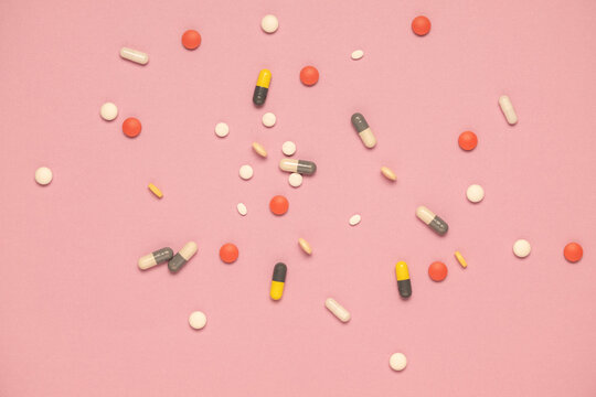 Multiple shapes and sizes of pharmaceutical medications on a pink background.  Polypharmacy concept.