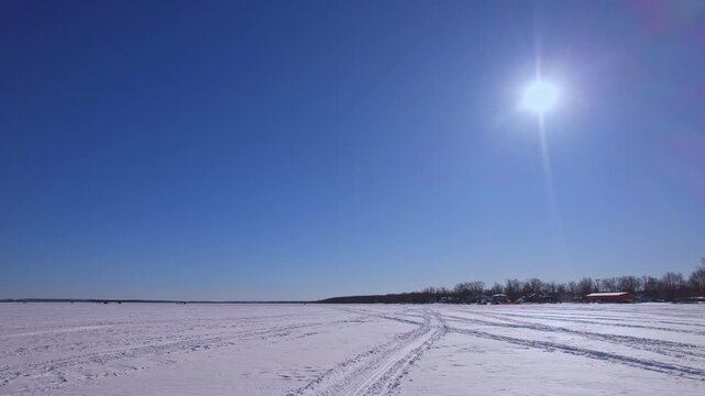 Aerial drone view at snowmobile, atv or ice fishing sled and snowdog tracks along the winter snowy lake Simcoe. Tourists and winter active recreation during ice fishing season. Blue sky.