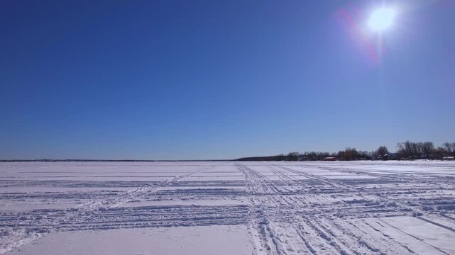 POV driving plate of driving snowmobile, atv or ice fishing sled and snowdog tracks along the winter snowy lake Simcoe. Tourists and winter active recreation during ice fishing season. Blue sky.