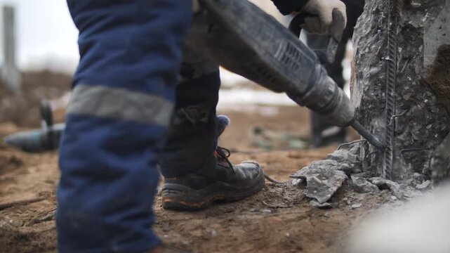 Worker breaking concrete pile with jackhammer during construction