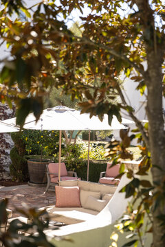 outdoor patio seating with umbrella, orange tile floor, blurry foreground looking through tree