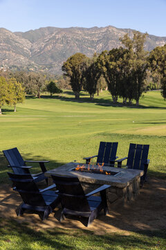 Chairs around a rectangle stone firepit next to a luxury golf course