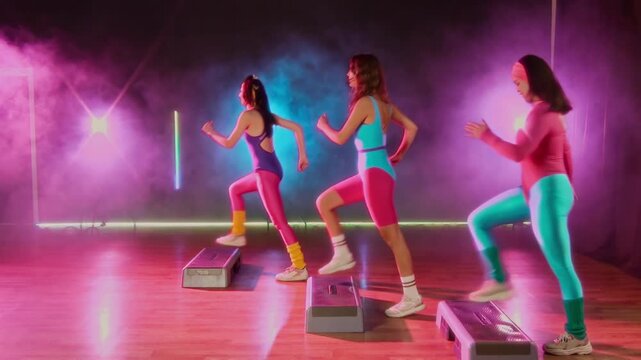 Wide shot with handheld zoom effect of three girls in colorful leotards and leggings exercising at step aerobics class with choreographed moves, in vibrant neon light and smoke, vintage VHS camcorder