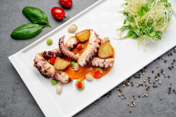 Seafood dish with octopus, potatoes, and vegetables on a white plate. A plate holds octopus cooked with potatoes, surrounded by cherry tomatoes and fresh greens, ready to eat. © white78