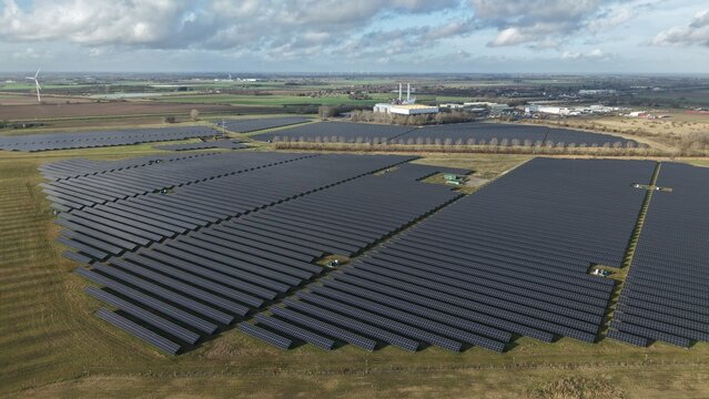 Aerial view of solar panels gleaming under a vast sky, contrasting with the distant industrial buildings, Sutton Bridge, Sutton Bridge, United Kingdom.