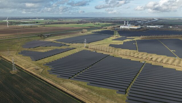 Aerial view of solar panels stretching across the landscape towards the distant power station under a sky of mottled clouds, Sutton Bridge, Sutton Bridge, United Kingdom.