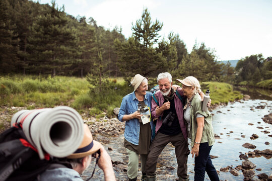 Senior friends laugh while hiking by forest river