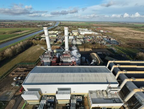 Aerial view of the power station's towering chimneys release faint plumes into the expansive blue sky above Centenary Way, Sutton Bridge, United Kingdom.