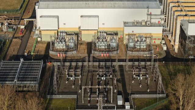 Aerial view of power station complex with its intricate network of transformers and electrical equipment, contrasting with the surrounding trees, Sutton Bridge, United Kingdom.