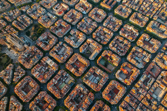 Aerial sunrise view of Barcelona showcasing the Eixample district with its octagonal residential blocks and precise urban grid. Soft morning light reveals the scale and structure of the city skyline