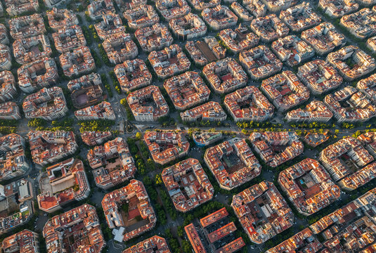Wide aerial sunrise view of Barcelona revealing the extensive Eixample grid stretching across the city. The orderly urban layout contrasts with the soft colors of early morning light