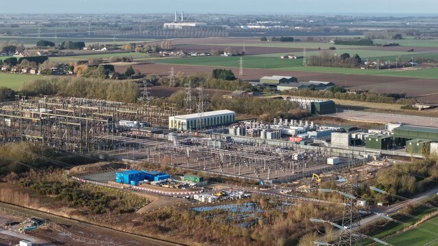 Aerial view of a power substation amidst the flat landscape, where metallic structures contrast with the earthy tones of the surrounding fields, Wisbech, United Kingdom.