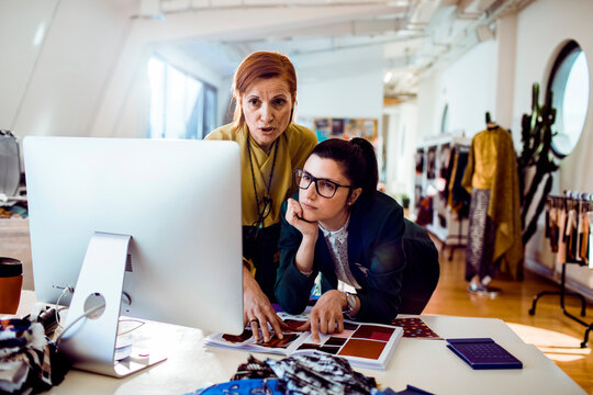 Two fashion designers collaborating at computer in modern studio