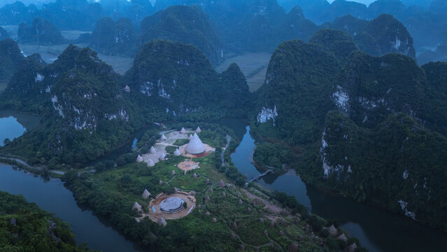 Aerial view of the misty landscape with striking limestone karsts rising above the winding river and the distinct structures below, Hoa Lu, Ninh Binh, Vietnam.