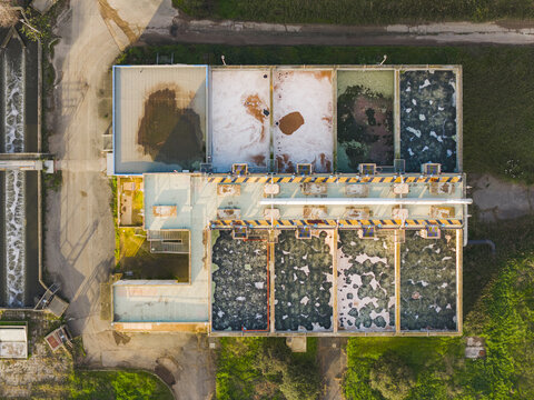 Aerial view of industrial pools reflecting mottled surfaces in varied hues, framed by green vegetation, Rome, Lazio, Italy.