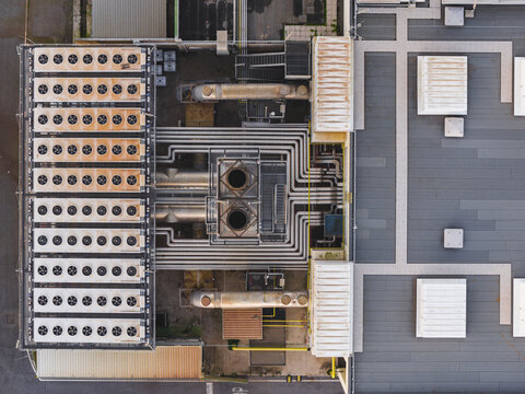 Aerial view of industrial infrastructure with complex piping and cooling systems, a stark contrast of metal against flat rooftops, Rome, Lazio, Italy.